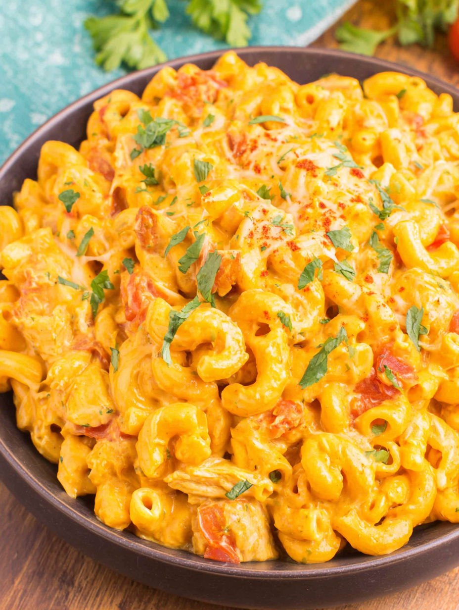 A bowl of macaroni and cheese with chicken and tomatoes.