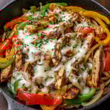 A skillet of chicken cheesesteak with peppers and onions.