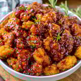 A bowl of orange chicken with a green herb on top.