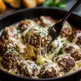 A spoon is in a bowl of cheesy meatballs.
