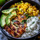 A bowl of food with rice, chicken, corn, and avocado.