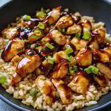 A bowl of rice with chicken and sauce.
