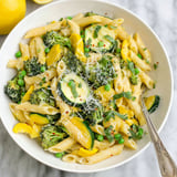 A bowl of pasta primavera with broccoli, zucchini, and peas.