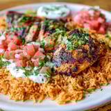 A plate of grilled chicken with rice and tomatoes.