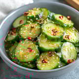 A bowl of cucumber salad with red peppers and sesame seeds.