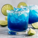 A blue margarita with lime wedges.