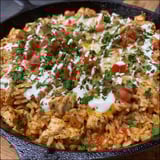 A skillet filled with chicken, cheese, and rice.