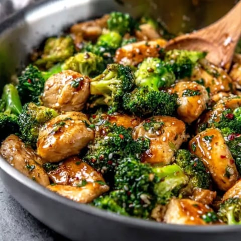 A pan of chicken and broccoli with a wooden spoon in it.