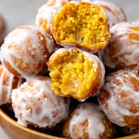 A bowl of pumpkin donut holes with icing.