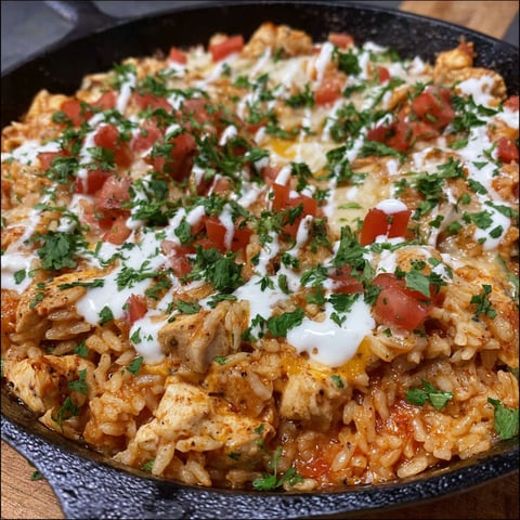 A skillet filled with chicken, cheese, and rice.